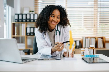 Sağlık uzmanı diz anatomisini açıklıyor. Tıbbi bir ortamda bir model kullanarak, tıbbi danışmanlık ve hasta bakımını vurguluyor.