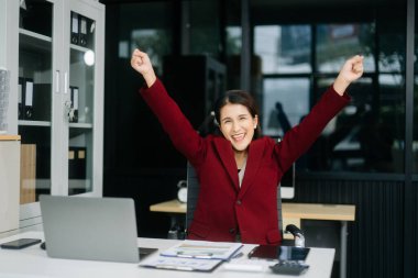 Genç, mutlu, çekici Asyalı kadın ofis çalışanı. Takım elbiseli, ofiste oturuyor.