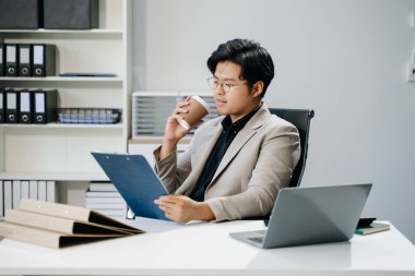 Genç Asyalı iş adamı laptopla çalışıyor ve kahve içiyor. 
