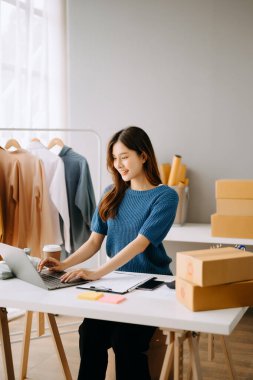 Asyalı terzi kadın terzi atölyesinde giysiler üzerinde çalışıyor. Güzel genç bayan moda tasarımcısı gülümsemesi ve stüdyo başarısından sonra