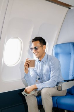 Asyalı işadamı uçak koltuğunda kahve içiyor. 