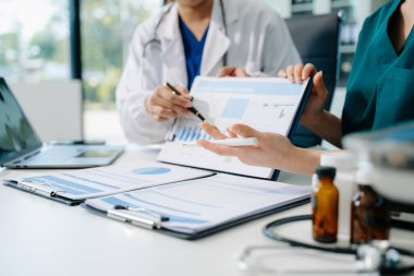 Tıbbi ekip, beyaz laboratuvar önlüklü ve ameliyat önlüklü doktorlarla toplantı yapıyor. Masada oturmuş, internette çalışan hastaları tartışıyorlar. Tıp endüstrisinde bilgisayar kullanıyorlar.