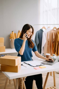 Startup small business SME, Entrepreneur owner woman using smartphone or tablet taking receive and checking online purchase shopping order to preparing pack product box.