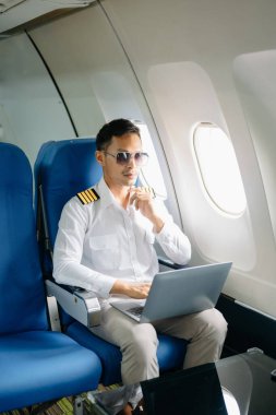 Yolcu koltuğunda dizüstü bilgisayar kullanarak gülümseyen Asyalı erkek pilot. 