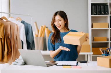 Startup small business SME, Entrepreneur owner woman using smartphone or tablet taking receive and checking online purchase shopping order to preparing pack product box.