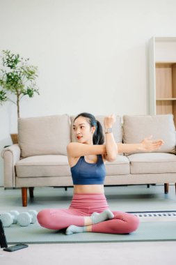 Genç bir kadın yoga yapıyor ve minder üzerinde esniyor, sağlığını, motivasyonunu ve modern bir ev ortamında sağlıklı ve aktif bir yaşam tarzını gösteriyor.