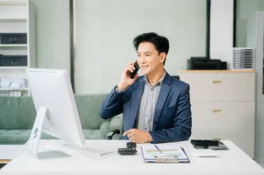 Asyalı işadamı tabletleri, laptopları ve ofiste yaptıkları işlerden memnun ve memnun.