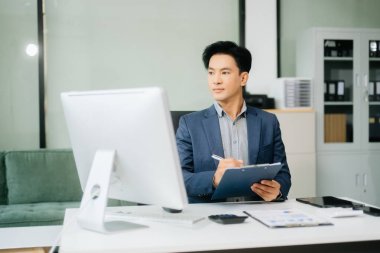 Çalışan not defteri, tablet ve dizüstü bilgisayarla çalışan genç Asyalı işadamı akıllı telefon, tablet ve dizüstü bilgisayarla konuşuyor.