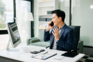 Asyalı işadamı tabletleri, laptopları ve ofiste yaptıkları işlerden memnun ve memnun.