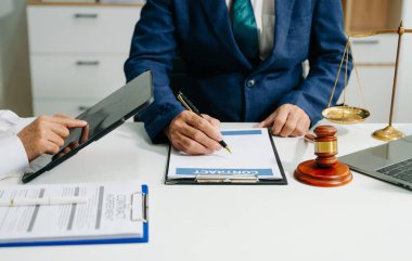 İş adamı ve avukatın orta kesimi bir ofiste kontrat belgelerini tartışıyor ve masasında büyük bir adalet terazisi bulunuyor. Hukuk kavramı, hukuk hizmetleri, mesleki danışmanlık ve adalet
