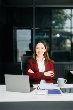 Çalışan not defteri, tablet ve dizüstü bilgisayarla çalışan Asyalı genç iş kadını akıllı telefon, tablet ve laptop video arama vergisi ile konuşuyor