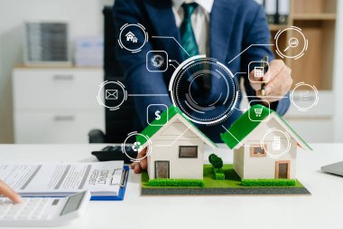 Emlak komisyoncusunun bir ofis ortamında ev modeli ve ipotek kredisi belgeleriyle anlaşma imzalama konusunda karar alma sürecini desteklemek için müşteriye danışmanlık yapan orta kesimi