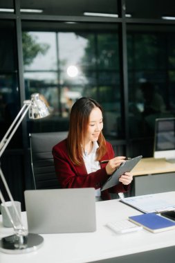 Çalışan not defteri, tablet ve dizüstü bilgisayarla çalışan genç Asyalı iş kadını akıllı telefon, tablet ve dizüstü bilgisayarla konuşuyor. 