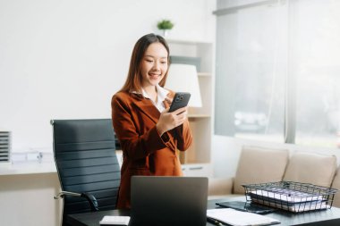 Genç ve güzel bir kadın, modern ofisin beyaz çalışma masasında otururken tablet ve dizüstü bilgisayarında yazıyor.