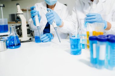 Yüksek teknolojili bir laboratuvarda iki bilim adamı biyokimyasal örnekleri analiz ediyor, mikro pipetler kullanıyor ve hassas bir şekilde gelişmiş tıbbi araştırmalar yürütüyorlar.