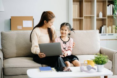 Neşeli anne ve kız kanepede güzel vakit geçiriyorlar, gülümsüyorlar ve dizüstü bilgisayar kullanıyorlar. Aile teması için mükemmel.