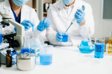 Yüksek teknolojili bir laboratuvarda iki bilim adamı biyokimyasal örnekleri analiz ediyor, mikro pipetler kullanıyor ve hassas bir şekilde gelişmiş tıbbi araştırmalar yürütüyorlar.