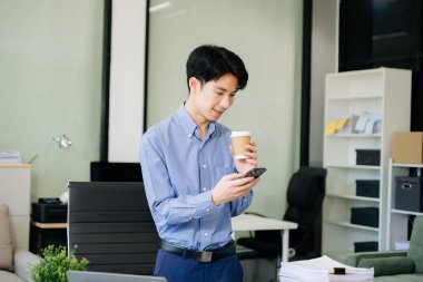 Genç iş adamı ofiste dizüstü bilgisayarla, tabletle çalışıyor ve kağıda not alıyor..