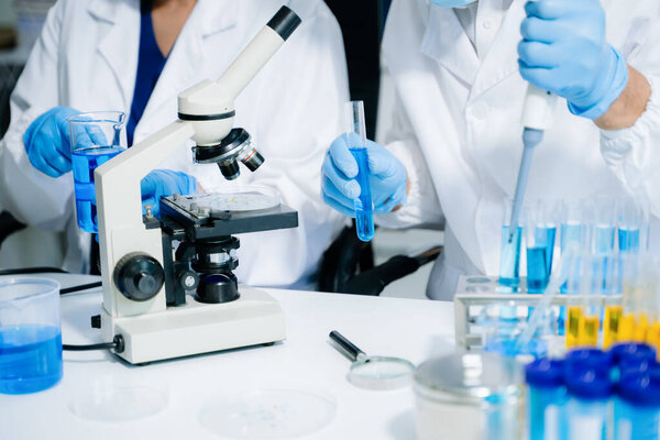 учёные в лабораторных халатах, проводящие исследования, обрабатывающие стекло и работающие с химикатами в современной высокотехнологичной лаборатории