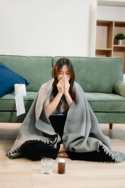 Kanepede battaniyeyle kaplanmış, grip belirtileri gösteren genç bir Asyalı kadın. Hastalık, sağlık ve iyileşme kavramı. 