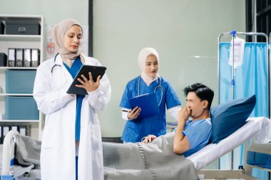 Dijital tablet kullanan, takım çalışması, profesyonellik ve sağlık hizmetlerini sergileyen doktorlar hastane koğuşundaki bir hastayla ilgileniyorlar.