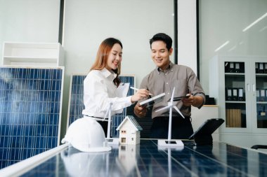 İki Asyalı mühendis, modern bir ofis ortamında yenilik ve sürdürülebilirliği tartışan bir güneş ve rüzgar enerjisi projesinde işbirliği yapıyorlar..