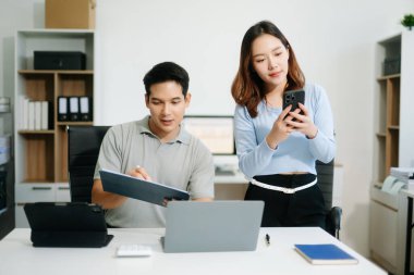 İki iş adamı akıllı telefondan konuşuyor ve ofiste dizüstü bilgisayar kullanıyorlar.