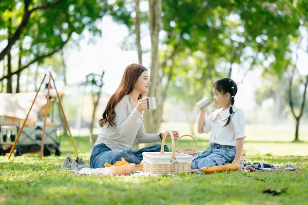 Asyalı bir anne ve kızı güneşli bir günde bahçede piknik yapıyorlar.