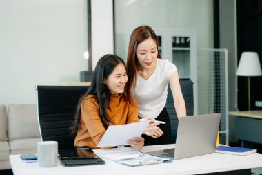 Businesswomen work and discuss their business plans. A woman employee explains and shows her colleague the results paper in modern office