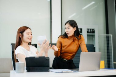 Ofiste dizüstü bilgisayarla çalışan iki yöneticiden oluşan bir iş ekibi. Genç Asyalı iş kadını yöneticisi proje gösteriyor.
