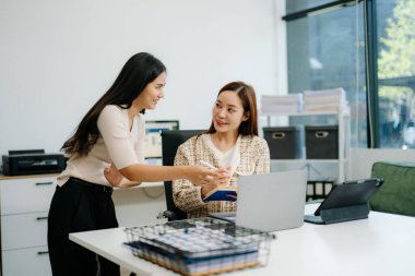 Ofiste dizüstü bilgisayarla çalışan iki yöneticiden oluşan bir iş ekibi. Genç Asyalı iş kadını yöneticisi proje gösteriyor.