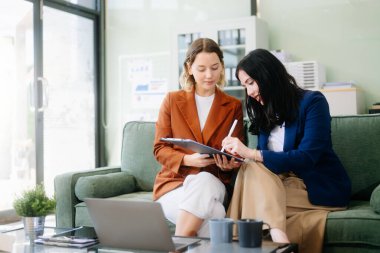 Profesyonel bir ofiste tabletle strateji kuran iki iş kadını. Bu modern işbirliği konseptiyle takım çalışmasını, liderliği ve yeniliği vurgula.