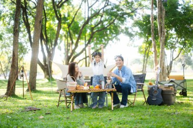 Aile yaz kampını kahve ve yiyecek kahvaltısıyla sever. Ebeveynler ve çocuklar piknik sırasında ve el kol hareketleri yaparken dışarıda kaynaşıyorlar. 
