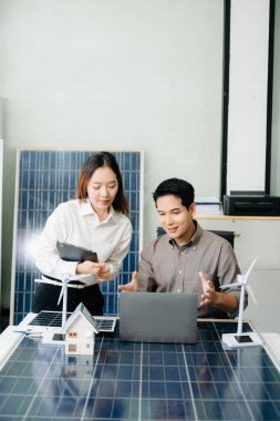 İki Asyalı mühendis, modern bir ofis ortamında yenilik ve sürdürülebilirliği tartışan bir güneş ve rüzgar enerjisi projesinde işbirliği yapıyorlar.. 