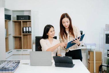 Businesswomen work and discuss their business plans. A woman employee explains and shows her colleague the results paper in modern office