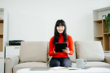 Genç Asyalı öğrenci evdeki kanepede oturuyor ve dijital tablet kullanıyor.