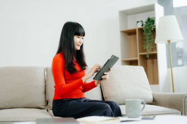 Genç Asyalı öğrenci evdeki kanepede oturuyor ve dijital tablet kullanıyor.  