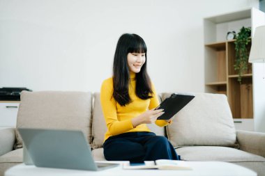 Genç Asyalı öğrenci evdeki kanepede oturuyor ve dijital tablet kullanıyor.  