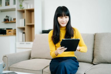 Genç Asyalı öğrenci evdeki kanepede oturuyor ve dijital tablet kullanıyor.  