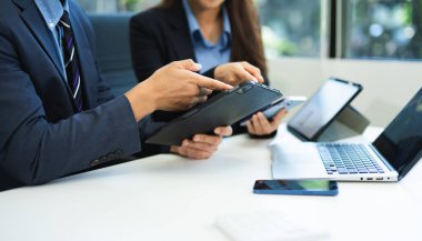 Ofis masasında akıllı telefon ve dizüstü bilgisayarı olan iş belgeleri ve sabah ışığında arka planda veri tartışması yapan iki iş arkadaşı.