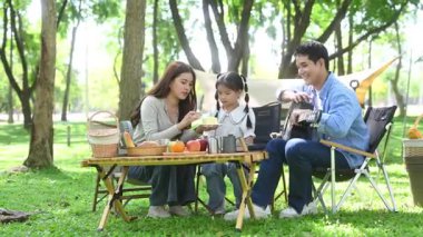 Aile yaz kampını kahve ve yiyecek kahvaltısıyla sever. Ebeveynler ve çocuklar piknik sırasında dışarı çıkıp gitar çalıyorlar.