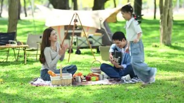 Aile yaz kampını kahve ve yiyecek kahvaltısıyla sever. Ebeveynler ve çocuklar piknik sırasında dışarı çıkıp gitar çalıyorlar.