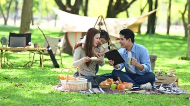 Aile yaz kampını kahve ve yiyecek kahvaltısıyla sever. Ebeveynler ve çocuklar piknik sırasında dışarıda birbirlerine bağlanıyorlar ve dijital tablet bilgisayar kullanıyorlar. 