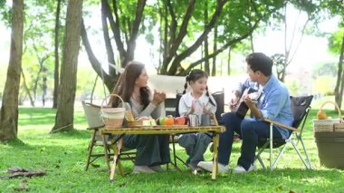 Aile yaz kampını kahve ve yiyecek kahvaltısıyla sever. Ebeveynler ve çocuklar piknik sırasında dışarı çıkıp gitar çalıyorlar.
