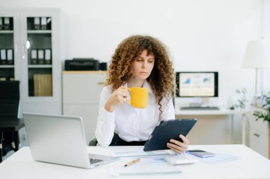 Modern ofiste başarılı bir iş kadını laptopta çalışıyor. Ofis masasında matematik finansmanı, vergi, rapor...