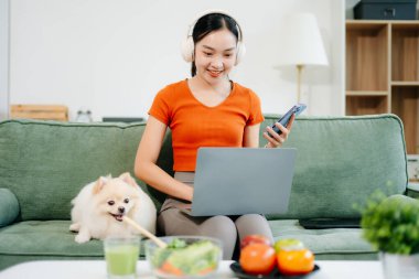 Evdeki kanepede köpeğiyle birlikte rahat bir şekilde oturuyor. Evdeki neşeli evcil hayvan, dizüstü bilgisayar kullanıyor.