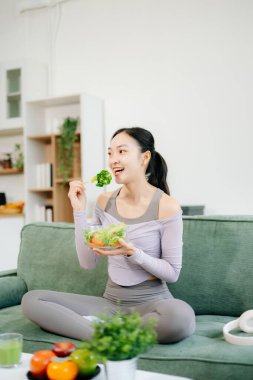Formda bir kadın meyve ve meyve suyu ile taze bir salatanın tadını çıkarır. Parlak, modern bir ev ortamında sağlıklı yaşam, beslenme ve canlılığı somutlaştırır.