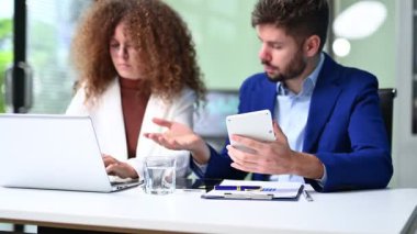 İşadamı ve işkadını, dizüstü bilgisayar ve hesap makinesi kullanarak ofiste iş birliği yapıyorlar.