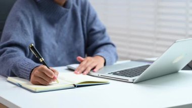 İş kadınlarının elleri dizüstü bilgisayarda çalışırken ve ofisteki not defterine not alırken.  