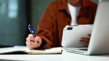 İş adamlarının elleri defterde not tutuyor ve ofiste dijital tablet üzerinde çalışıyor.